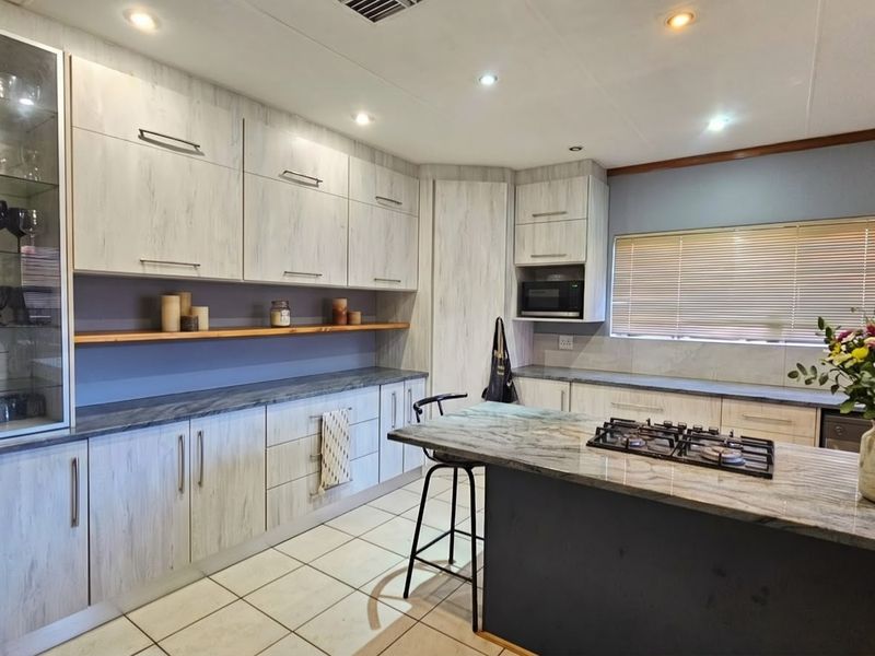 Modern kitchen featuring light wood-grain cabinetry, stone countertops, a central island with a gas hob, and integrated appliances with ample storage space.