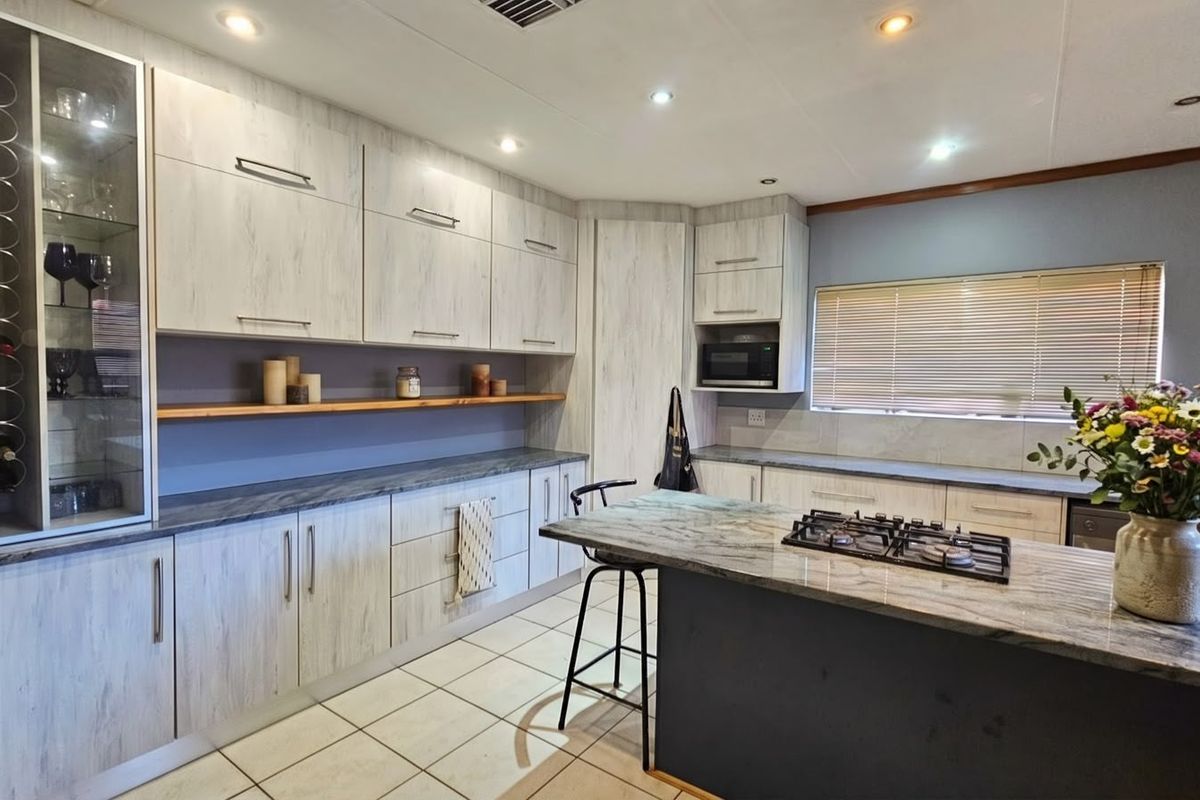 Modern kitchen featuring light wood-grain cabinetry, stone countertops, a central island with a gas hob, and integrated appliances with ample storage space.