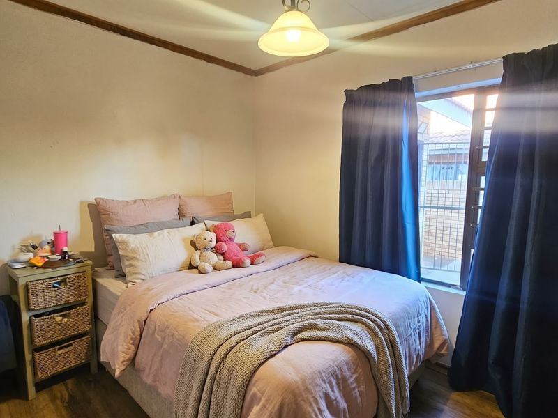 A standard bedroom featuring laminate flooring, a central light fixture, and a window with curtain tracks.