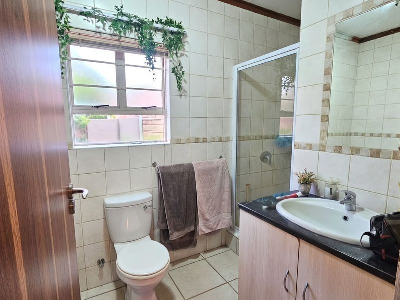 A functional bathroom featuring tiled walls and flooring, a shower enclosure, a vanity cabinet with a basin, and a wall-mounted mirror.