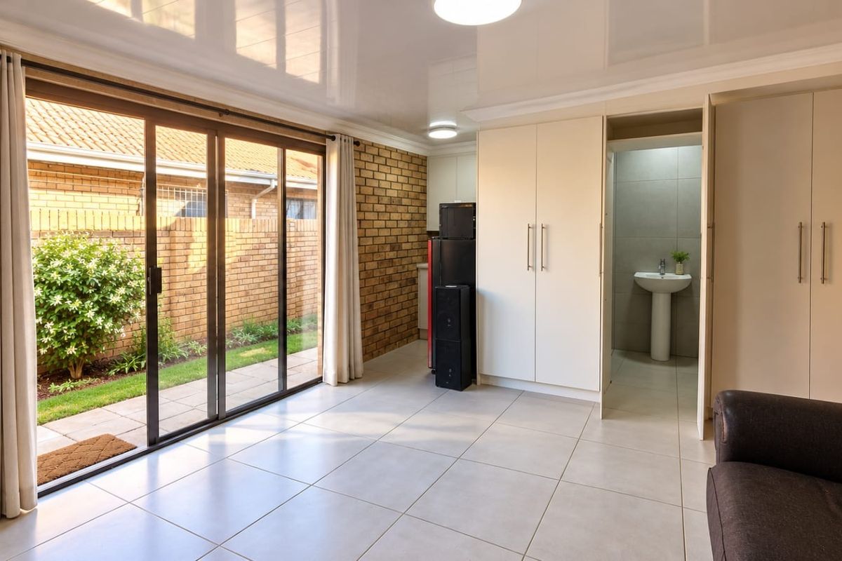 Bright living area featuring large sliding doors to the garden, tiled floors, exposed brick accents, and convenient built-in storage with an integrated basin area.