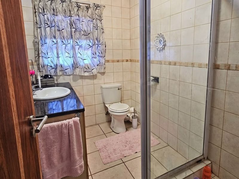 A functional bathroom featuring a vanity with granite countertop, a toilet, and a glass-enclosed shower with tiled finishes throughout.