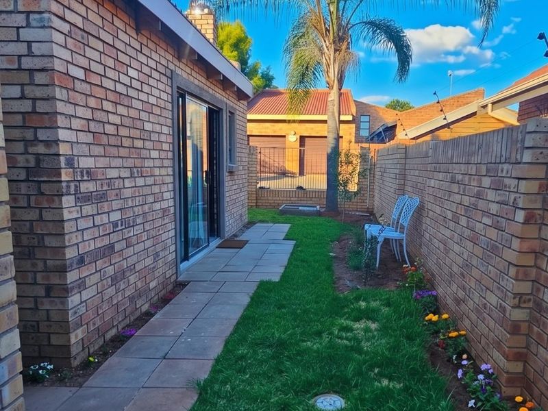 A well-maintained rear garden featuring a paved walkway, manicured lawn, and face brick boundary walls, providing a private outdoor space.