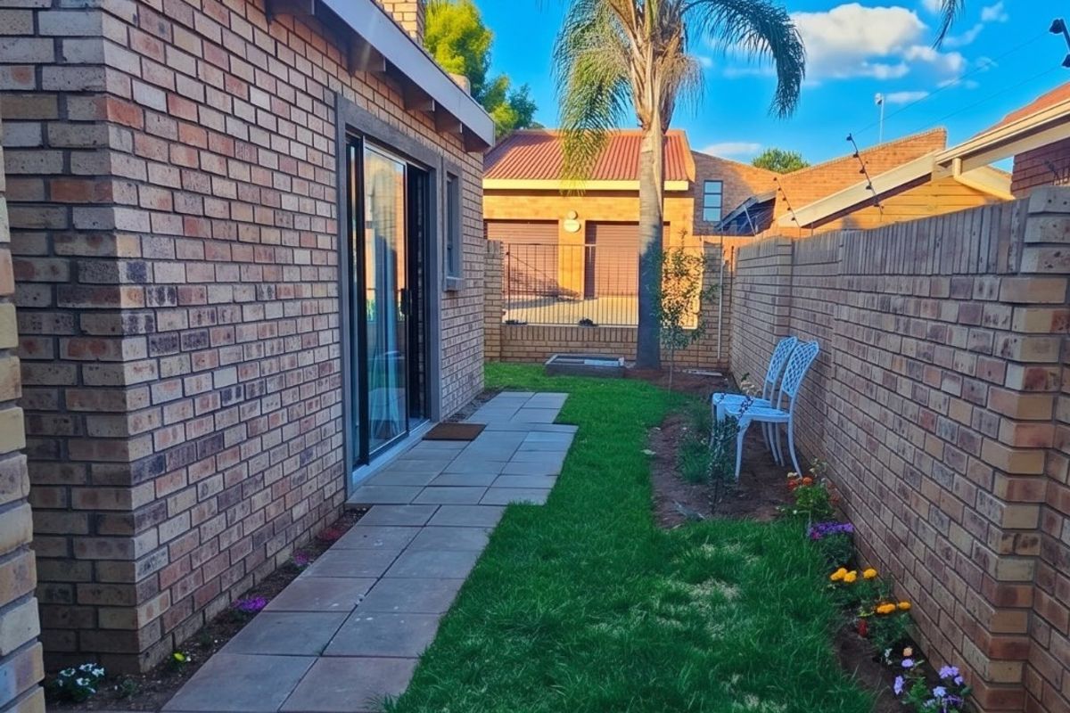 A well-maintained rear garden featuring a paved walkway, manicured lawn, and face brick boundary walls, providing a private outdoor space.