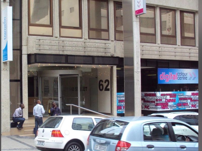 Front exterior view of a commercial office building featuring a revolving door entrance, concrete facade, and prominent street-level signage.