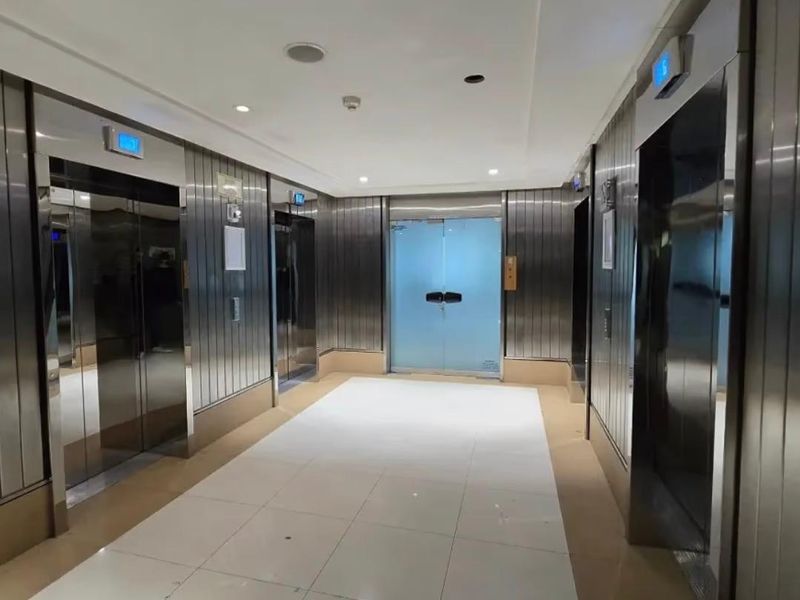 A modern office building elevator lobby featuring stainless steel elevator doors, tiled flooring, and a secure glass entrance door.