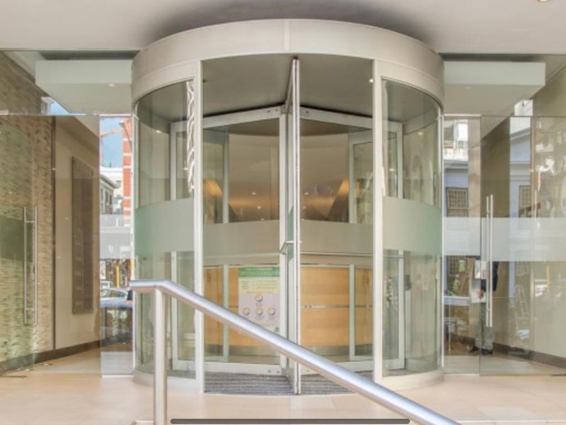 Modern office building entrance featuring a prominent revolving glass door, sleek glass facade, and clean tiled flooring.