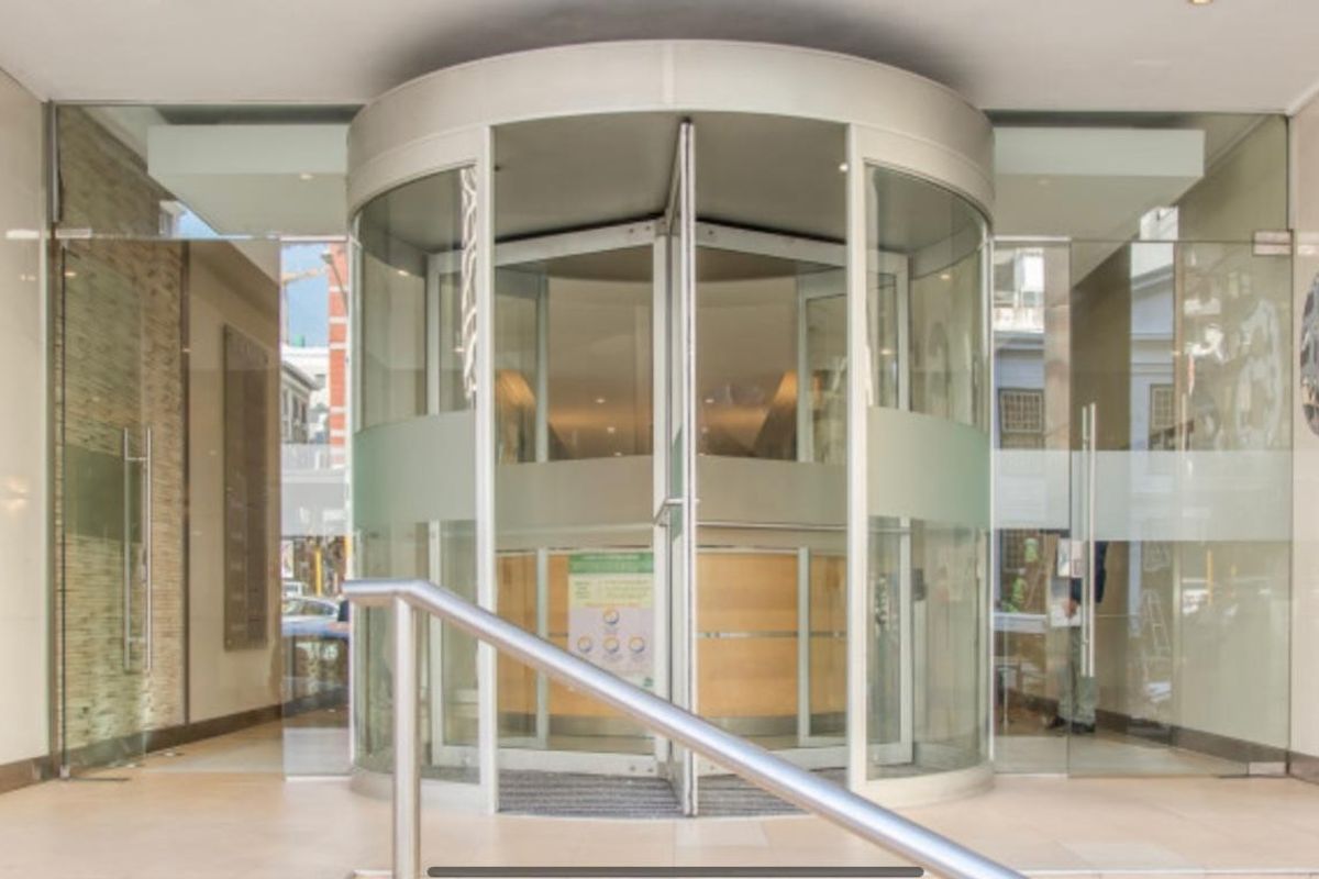 Modern office building entrance featuring a prominent revolving glass door, sleek glass facade, and clean tiled flooring.