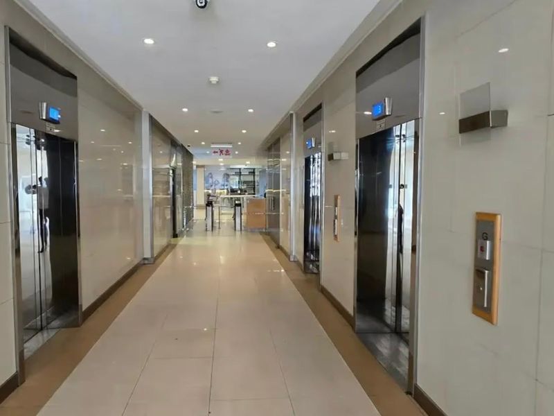 A modern office building elevator lobby featuring tiled flooring, polished wall cladding, and multiple elevator access points.
