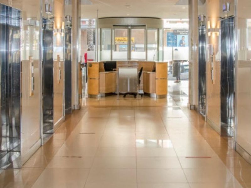 A professional office building lobby featuring a reception desk, multiple elevator banks, and polished tiled flooring with a modern revolving entrance door.