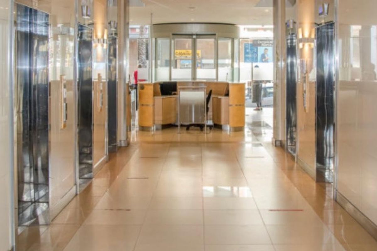 A professional office building lobby featuring a reception desk, multiple elevator banks, and polished tiled flooring with a modern revolving entrance door.