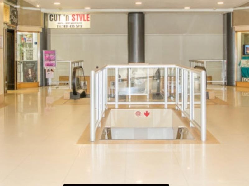 A bright, open-plan office or commercial lobby area featuring tiled flooring, central escalator access, and glass-fronted units.