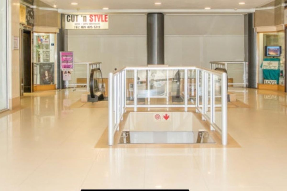 A bright, open-plan office or commercial lobby area featuring tiled flooring, central escalator access, and glass-fronted units.
