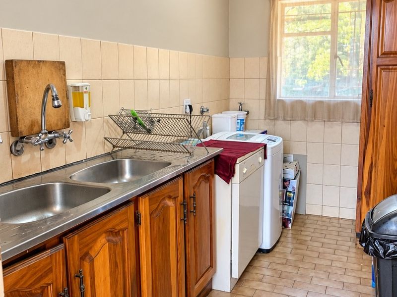 Functional laundry room featuring wooden cabinetry, a double stainless steel sink, tiled splashbacks, and tiled flooring with a window for natural light.