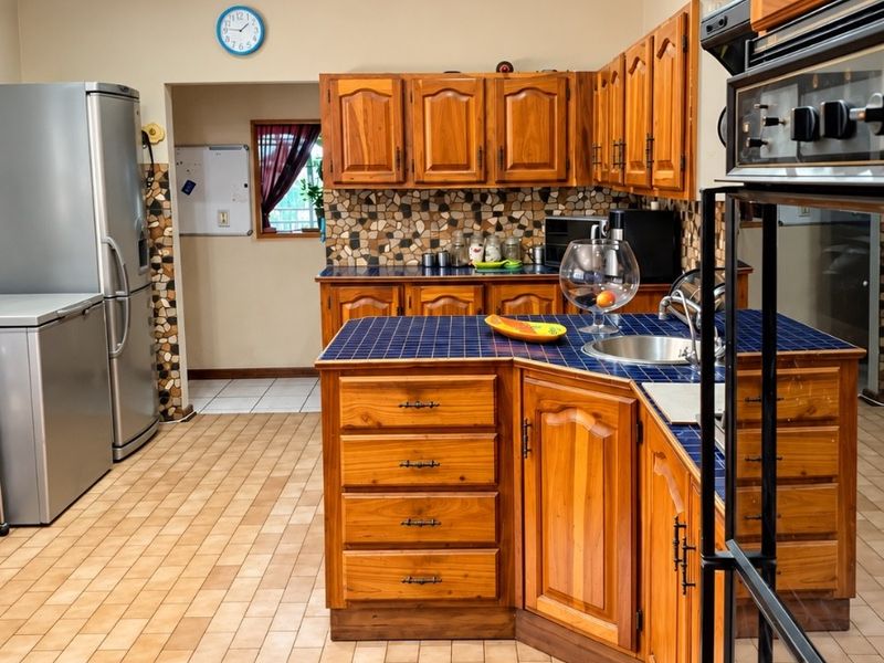 A functional kitchen featuring traditional wooden cabinetry, tiled countertops, a built-in oven, and a mosaic tile backsplash with tiled flooring throughout.