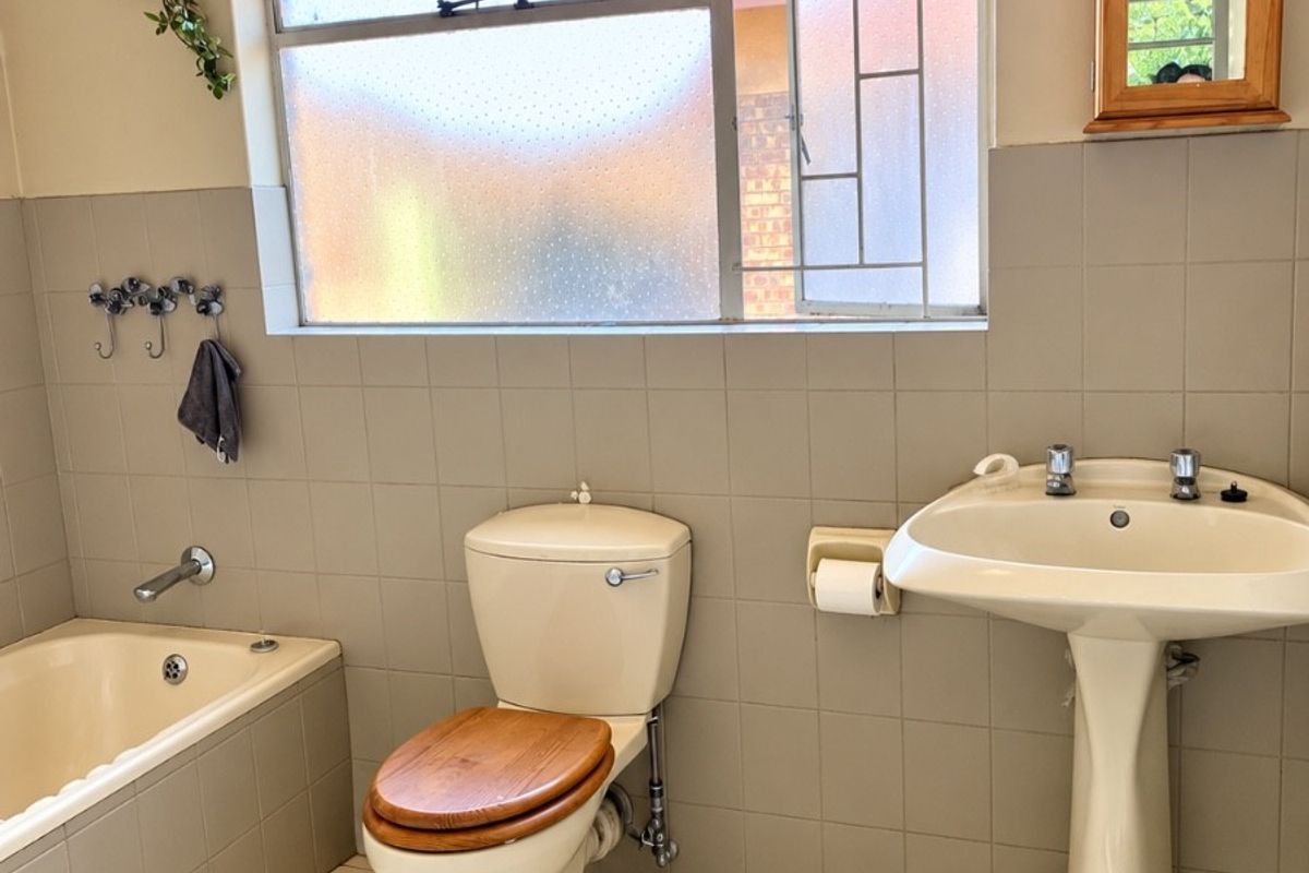 A functional bathroom featuring a pedestal basin, built-in bathtub, and toilet with neutral wall and floor tiling.