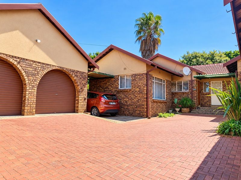 Front exterior view of a brick house featuring a double garage with arched openings and a spacious paved driveway.