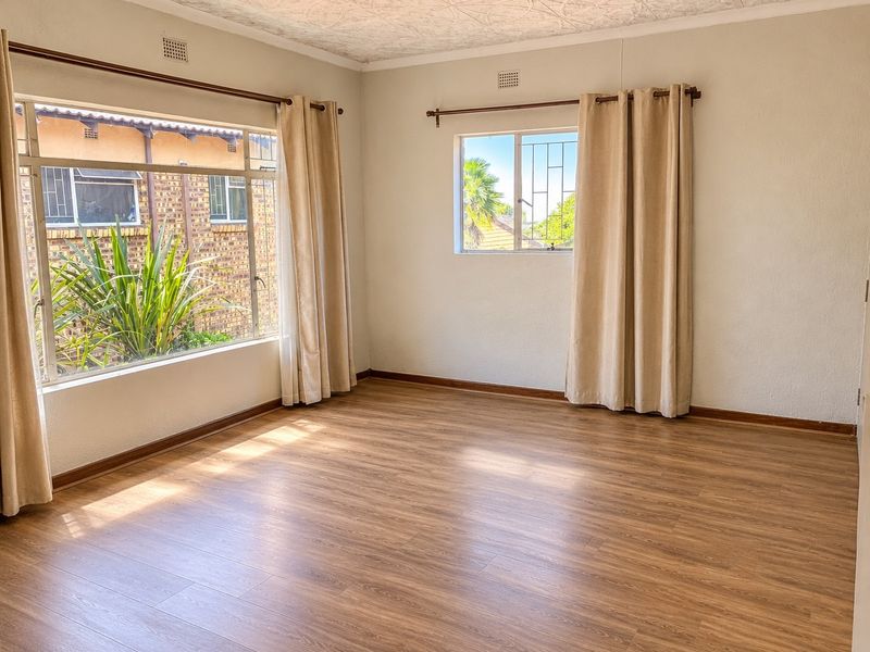 A bright and spacious living area featuring laminate flooring, textured ceilings, and large windows with security bars, offering a clean and neutral canvas.