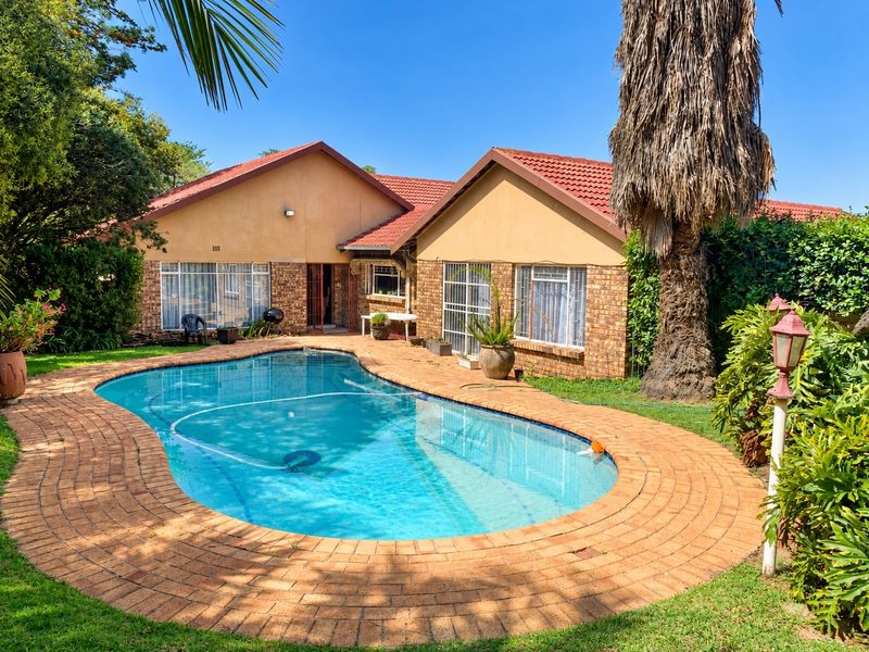 A private backyard featuring a swimming pool with a brick-paved surround, set against a house with a tiled roof and brick exterior.