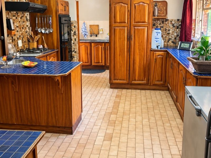 Spacious kitchen featuring traditional wooden cabinetry, blue tiled countertops, mosaic backsplash, and a functional layout with a separate scullery area.