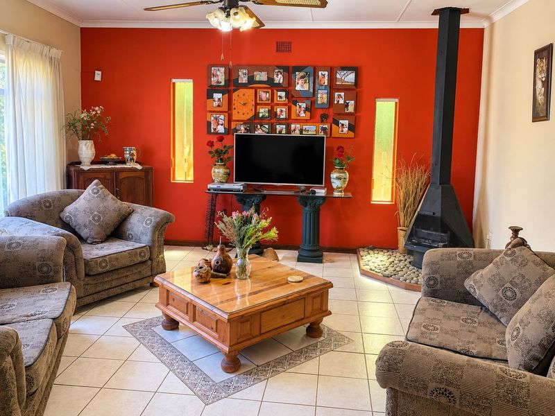A living room featuring tiled flooring, a prominent red accent wall, a freestanding fireplace, and vertical windows providing natural light.