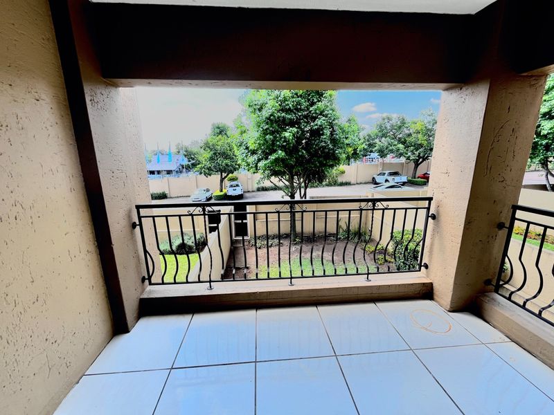 A covered balcony featuring tiled flooring and a wrought iron balustrade, overlooking a landscaped garden area.