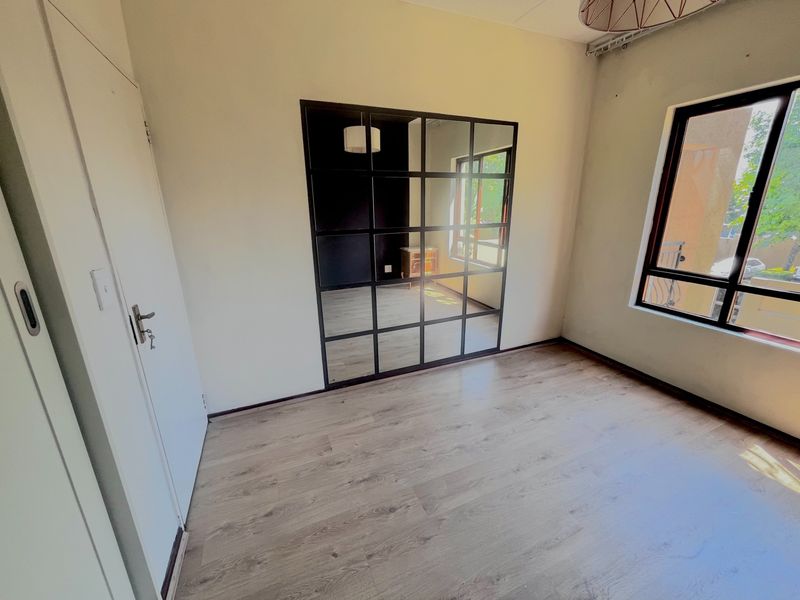 A bright, empty bedroom featuring modern laminate flooring, a large grid-pattern mirror wall feature, and natural light from the window.