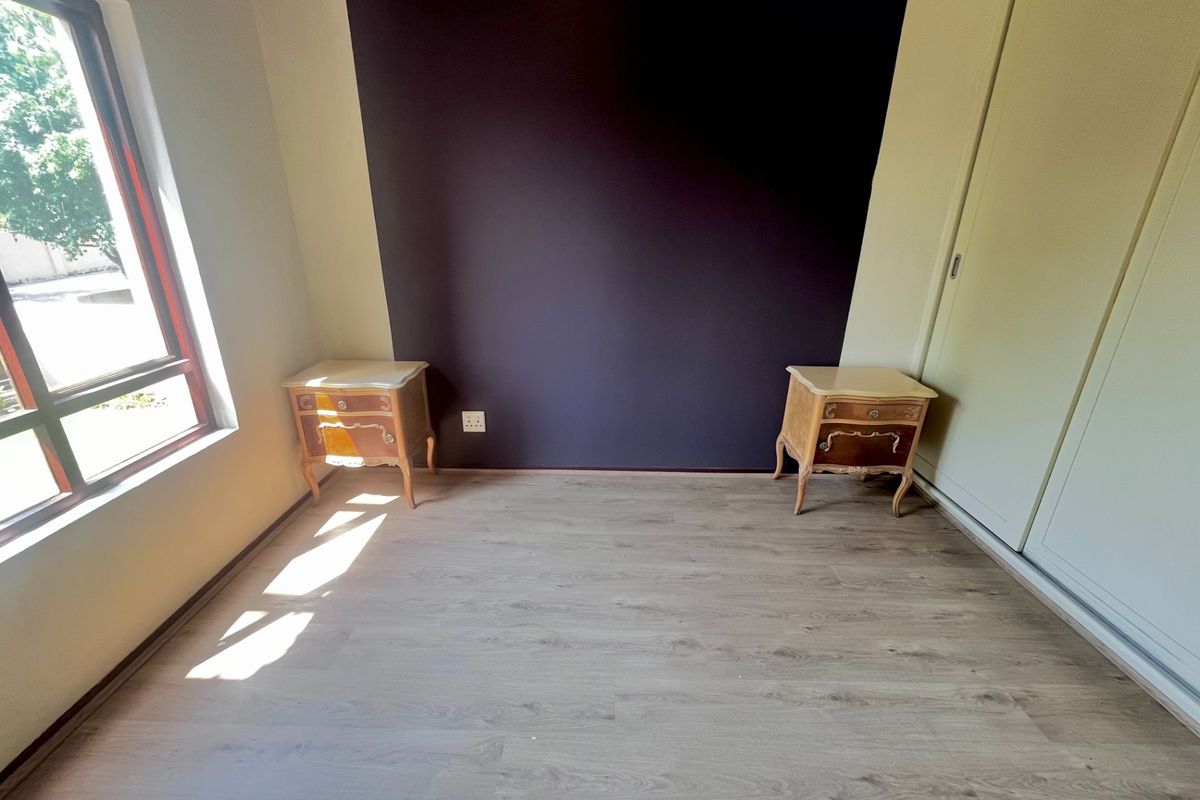 A bedroom featuring laminate flooring, a built-in wardrobe, and a dark accent wall, providing a clean and functional space.