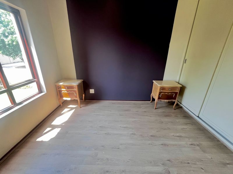 A bedroom featuring laminate flooring, a built-in wardrobe, and a dark accent wall, providing a clean and functional space.