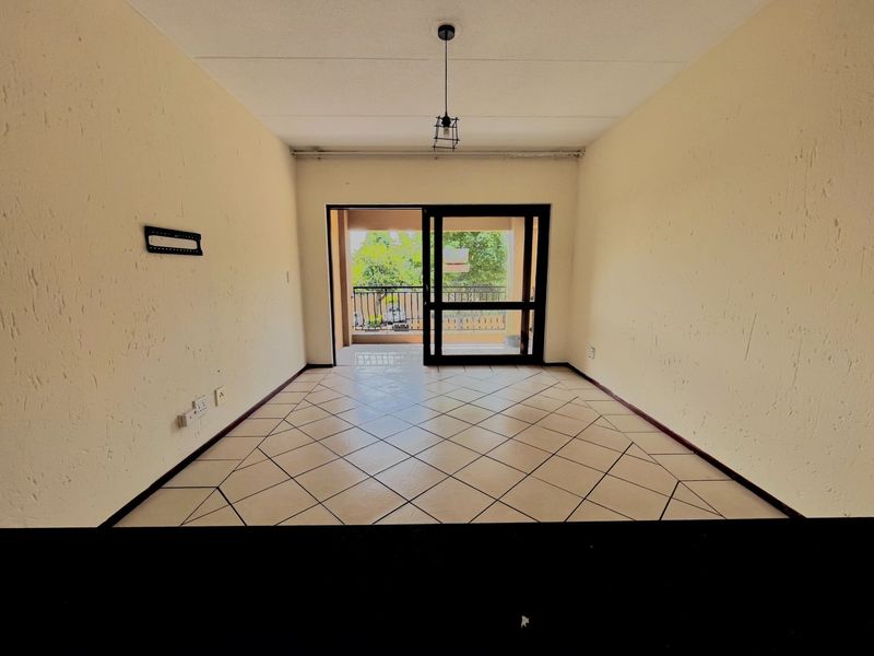 An empty, open-plan living area featuring tiled flooring, textured walls, and a sliding glass door providing direct access to a private balcony.
