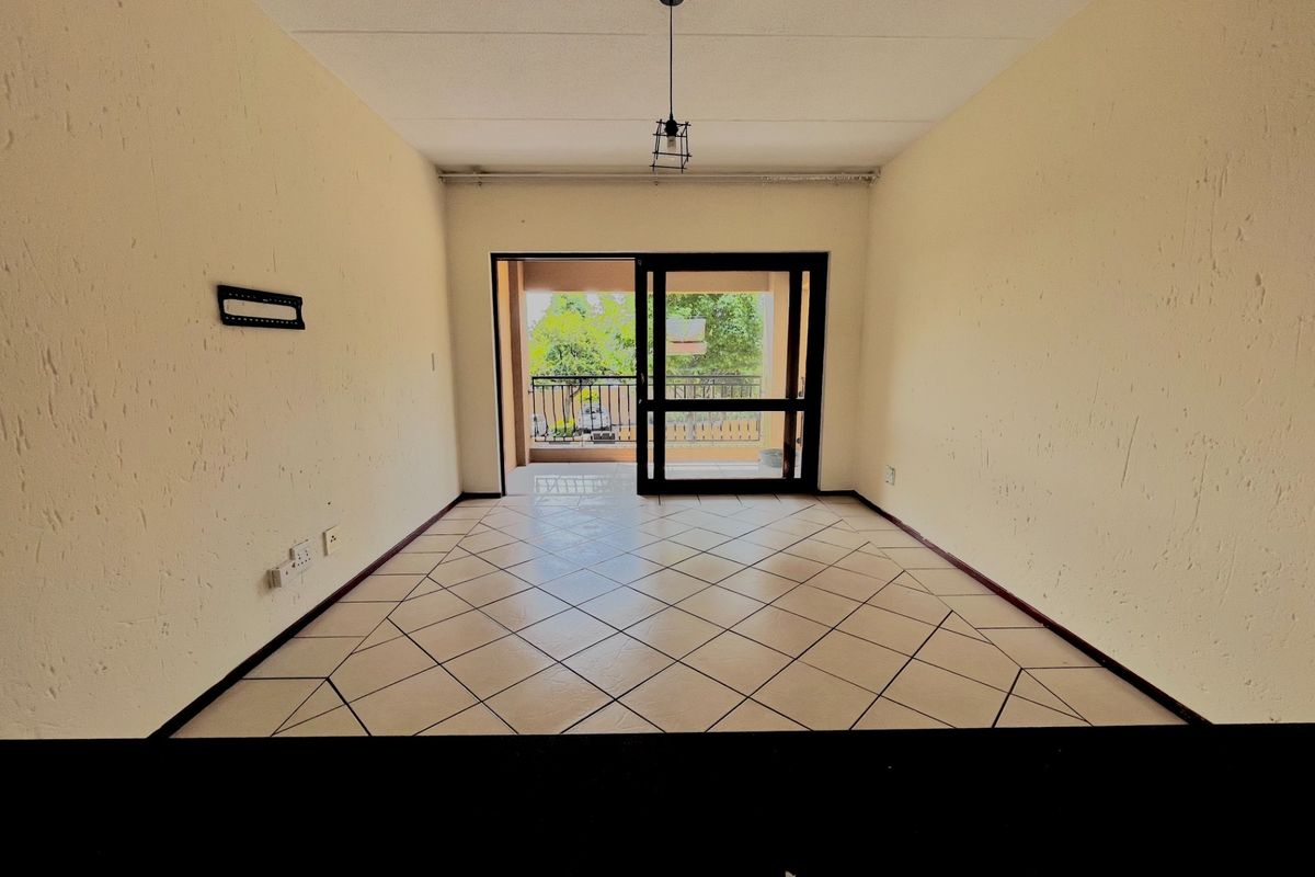 An empty, open-plan living area featuring tiled flooring, textured walls, and a sliding glass door providing direct access to a private balcony.