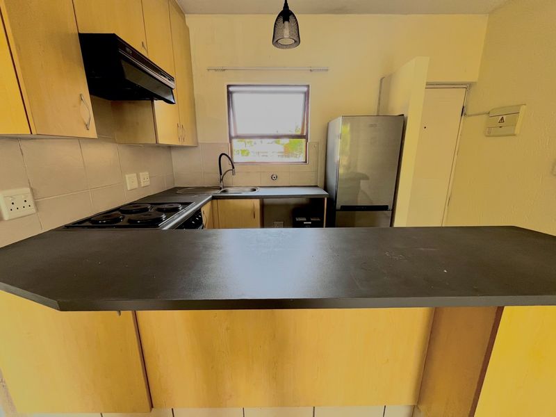 A functional kitchen featuring light wood cabinetry, a breakfast bar, electric hob, and tiled backsplash, offering a practical layout for daily meal preparation.
