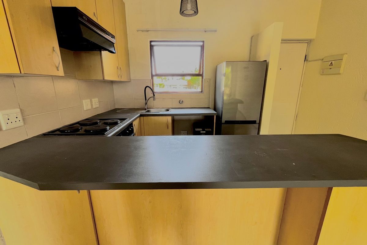 A functional kitchen featuring light wood cabinetry, a breakfast bar, electric hob, and tiled backsplash, offering a practical layout for daily meal preparation.