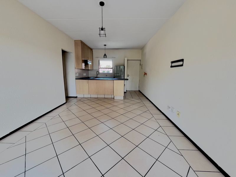 An open-plan living and kitchen area featuring tiled flooring, built-in cabinetry, and a functional layout, presenting a blank canvas for personalization.