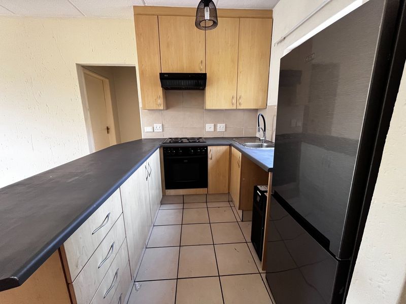 A functional kitchen featuring light wood-finish cabinetry, dark countertops, built-in oven with hob, and tiled flooring, offering a practical layout for daily use.