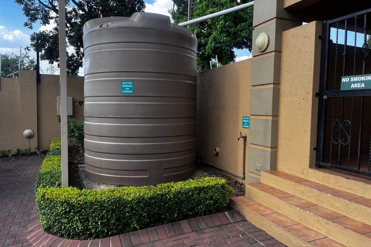 Exterior area featuring a large water storage tank, paved walkway, and tiled steps leading to a secure entrance gate.