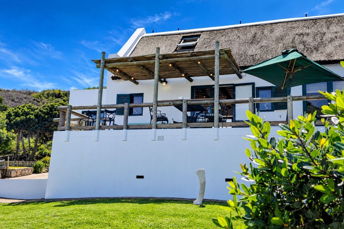 Rear elevation of a charming thatched-roof house featuring a raised timber deck with a pergola, overlooking a well-maintained garden.