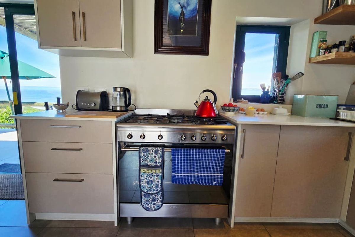 A functional kitchen featuring a stainless steel gas hob and oven, modern cabinetry, and floating shelves, with direct access to an outdoor patio area.