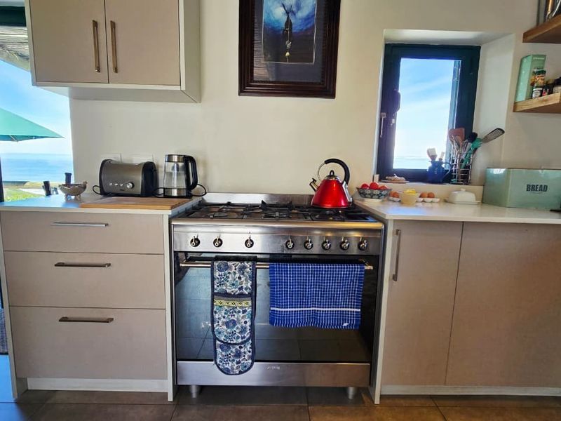 A functional kitchen featuring a stainless steel gas hob and oven, modern cabinetry, and floating shelves, with direct access to an outdoor patio area.