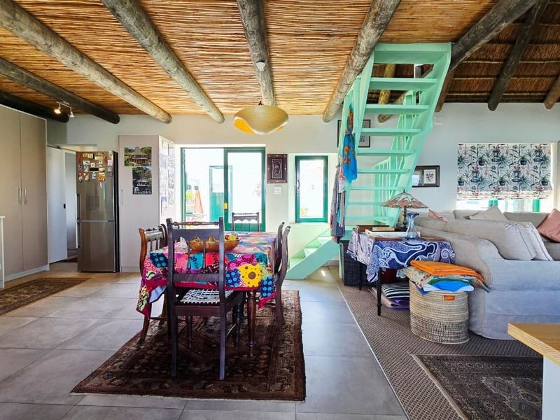 Spacious open-plan living area featuring a high thatch ceiling with exposed timber beams, tiled flooring, and a staircase leading to an upper level.