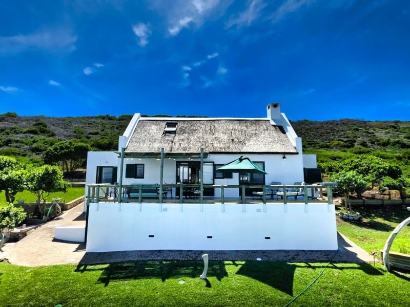 Rear view of a charming white cottage featuring a traditional thatched roof, a spacious timber deck, and a well-maintained garden setting.