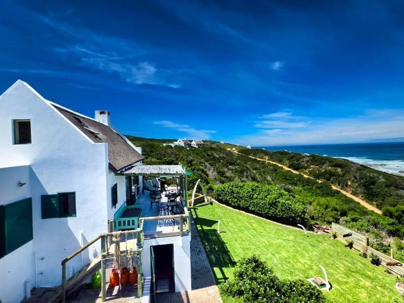 Rear view of a coastal property featuring a thatched roof, elevated timber deck, and a well-maintained garden overlooking the ocean.