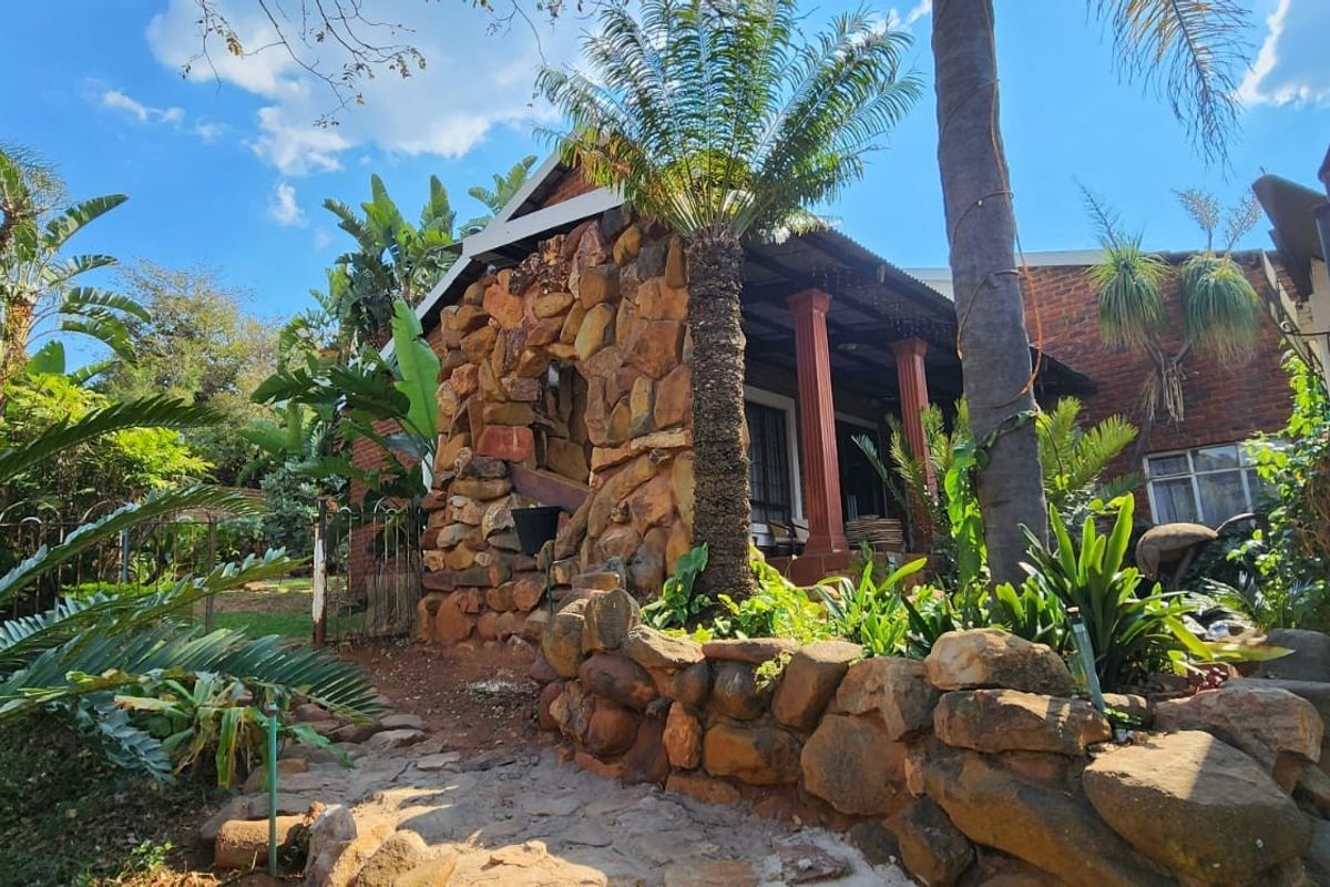 A rustic rear exterior view featuring stone-clad architectural elements, a covered patio area, and established garden landscaping.