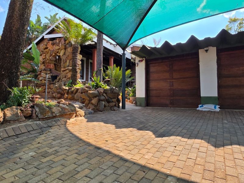 Front exterior view featuring a double garage with wooden doors, stone cladding accents, and a paved driveway area covered by a shade sail.