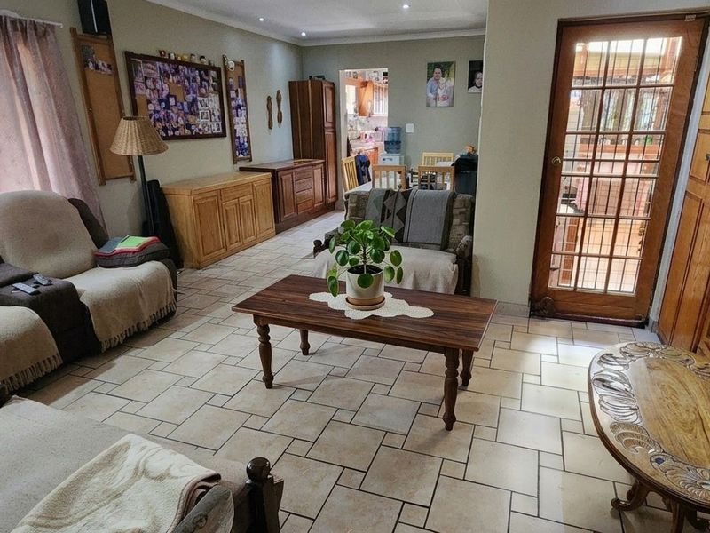 A spacious living room featuring tiled flooring, recessed lighting, and built-in wooden cabinetry, with direct access to an outdoor area through a glass-paned door.