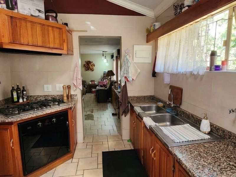 A functional kitchen featuring wooden cabinetry, granite countertops, a gas hob, built-in oven, and a double stainless steel sink with tiled flooring.