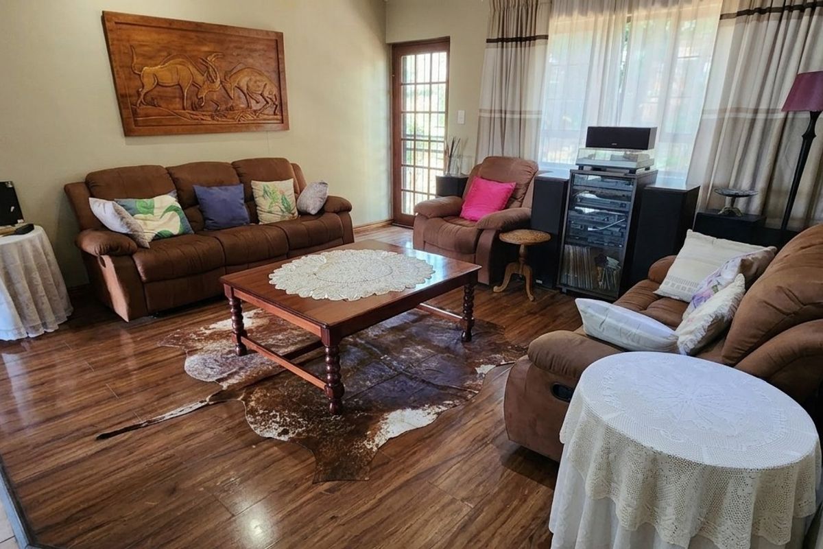 A comfortable living room featuring warm-toned laminate flooring, natural light from a large window, and direct access to the exterior via a glass panel door.