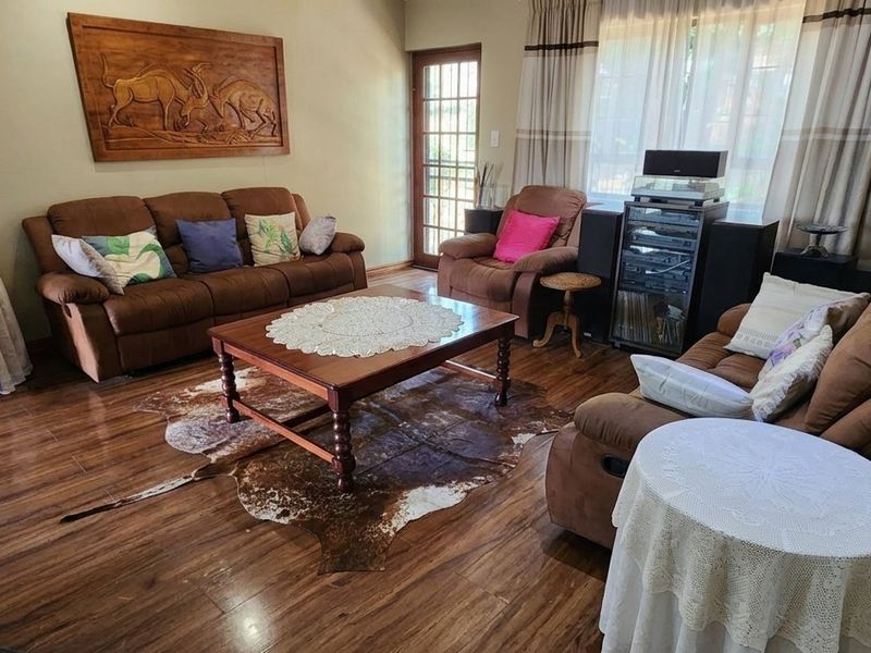 A comfortable living room featuring warm-toned laminate flooring, natural light from a large window, and direct access to the exterior via a glass panel door.