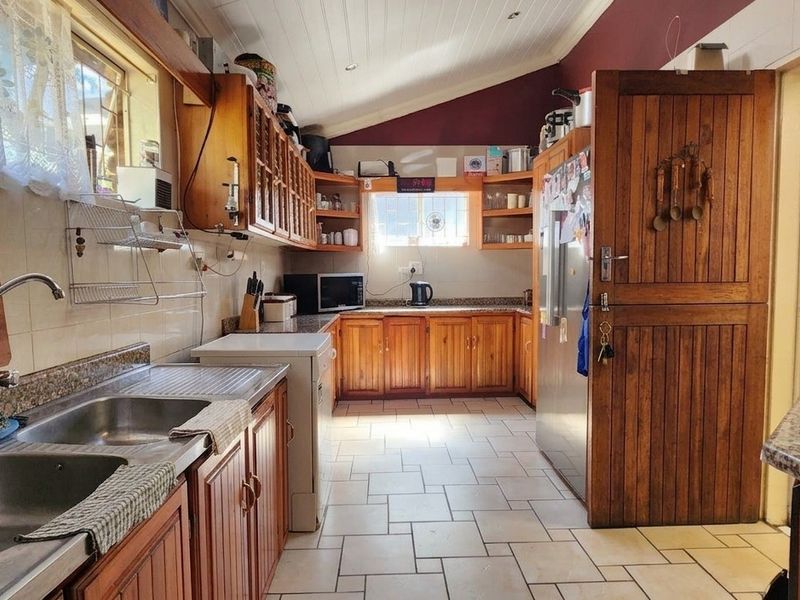 A functional kitchen featuring wooden cabinetry, granite countertops, a double stainless steel sink, and a gas hob, set under a vaulted ceiling.