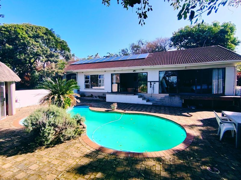 Rear exterior view featuring a swimming pool, paved patio area, and a house roof equipped with solar panels.